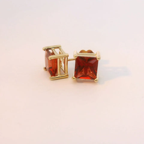 Gold tone earrings featuring rectangular red gemstones, front view.