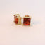 Gold tone earrings featuring rectangular red gemstones, front view.