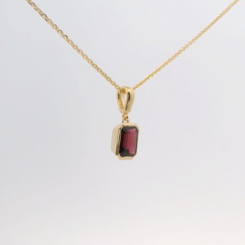 gold pendant with an emerald-cut red stone, side view