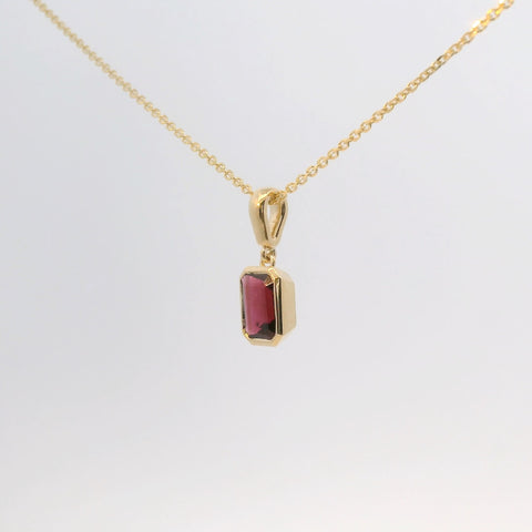 gold pendant with an emerald-cut red stone, angled view